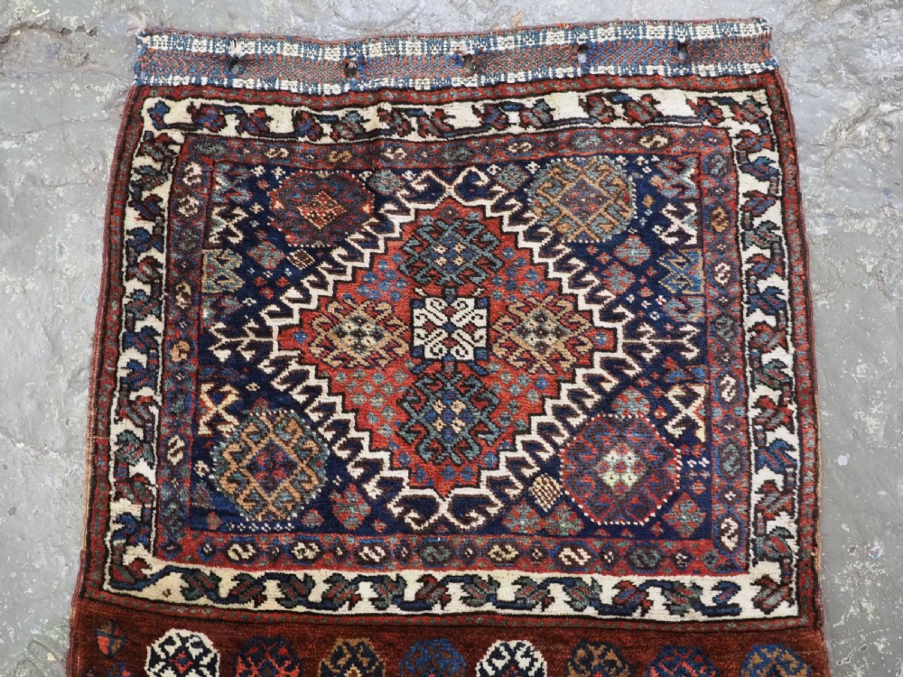 A late 19th-century South Persian hand-woven wool double saddle bag featuring geometric medallions, repeated guls, and stepped diamond patterns in shades of deep red, indigo blue, and ivory. View III