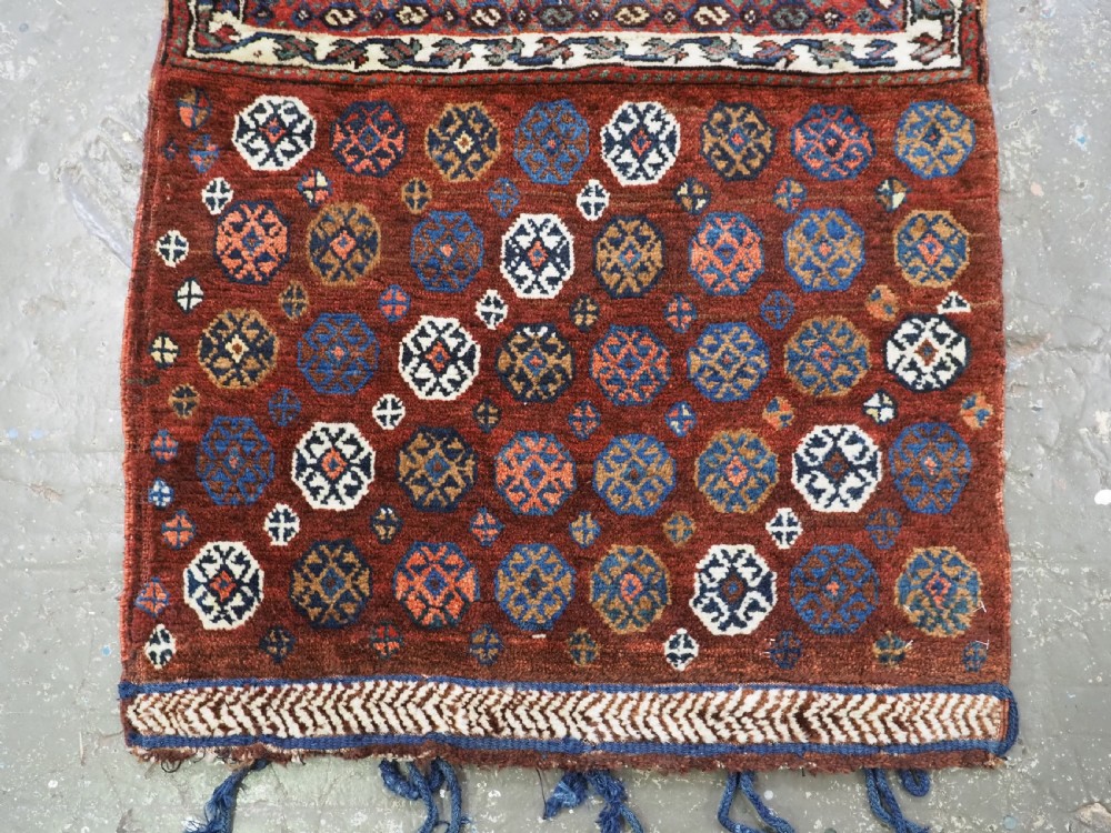 A late 19th-century South Persian hand-woven wool double saddle bag featuring geometric medallions, repeated guls, and stepped diamond patterns in shades of deep red, indigo blue, and ivory. View IV