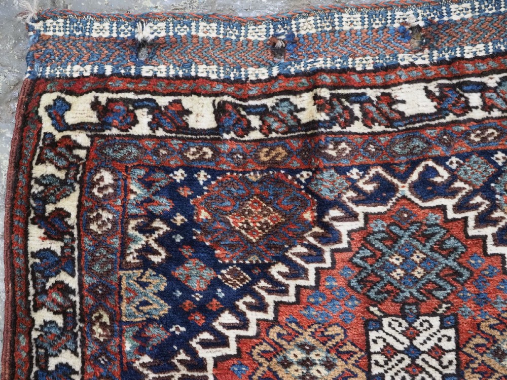 A late 19th-century South Persian hand-woven wool double saddle bag featuring geometric medallions, repeated guls, and stepped diamond patterns in shades of deep red, indigo blue, and ivory. View V