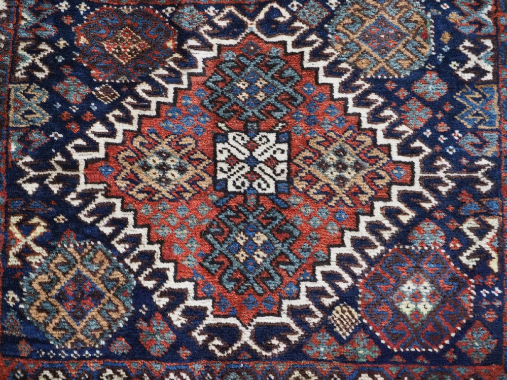 A late 19th-century South Persian hand-woven wool double saddle bag featuring geometric medallions, repeated guls, and stepped diamond patterns in shades of deep red, indigo blue, and ivory. View VI