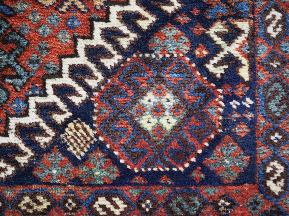 A late 19th-century South Persian hand-woven wool double saddle bag featuring geometric medallions, repeated guls, and stepped diamond patterns in shades of deep red, indigo blue, and ivory. View IX