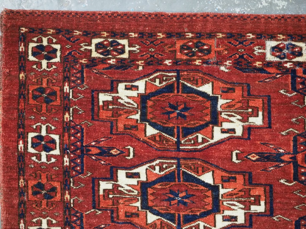 A rectangular hand-woven Tekke Turkmen wool textile featuring six octagonal guls on a deep red field with an intricate geometric border and long blue and red fringe along the bottom edge. View VII