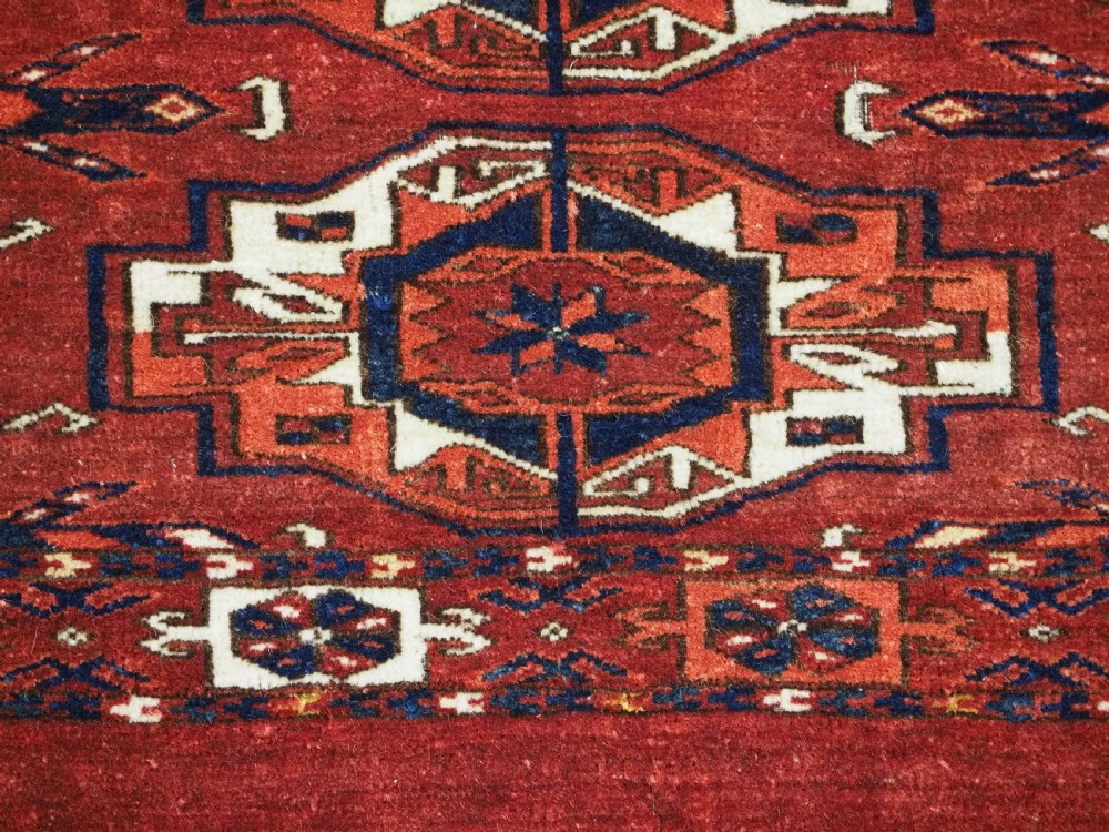 A rectangular hand-woven Tekke Turkmen wool textile featuring six octagonal guls on a deep red field with an intricate geometric border and long blue and red fringe along the bottom edge. View VIII