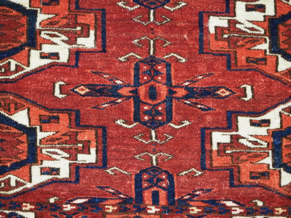 A rectangular hand-woven Tekke Turkmen wool textile featuring six octagonal guls on a deep red field with an intricate geometric border and long blue and red fringe along the bottom edge. View IX