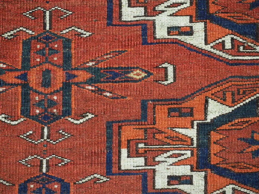 A rectangular hand-woven Tekke Turkmen wool textile featuring six octagonal guls on a deep red field with an intricate geometric border and long blue and red fringe along the bottom edge. View XII