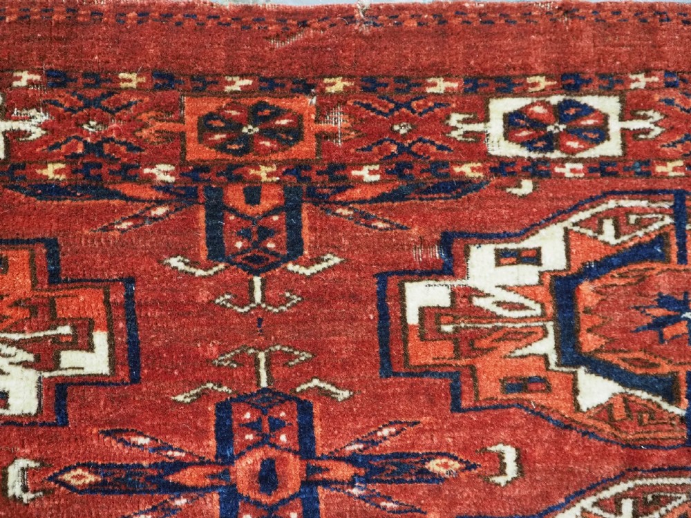 A rectangular hand-woven Tekke Turkmen wool textile featuring six octagonal guls on a deep red field with an intricate geometric border and long blue and red fringe along the bottom edge. View XIV