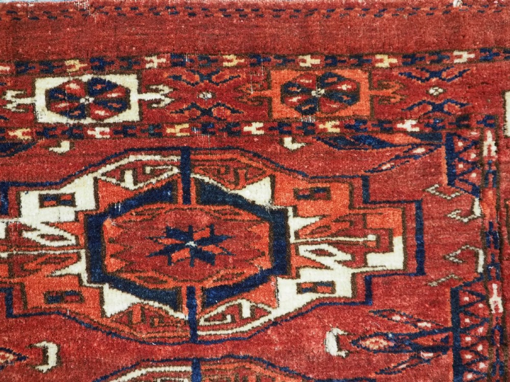 A rectangular hand-woven Tekke Turkmen wool textile featuring six octagonal guls on a deep red field with an intricate geometric border and long blue and red fringe along the bottom edge. View XV