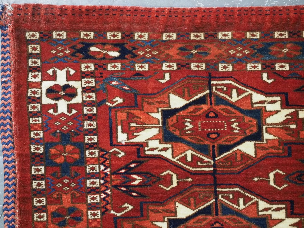 A horizontal handwoven wool Tekke Turkmen torba featuring six octagonal gul medallions on a deep red background with geometric borders and braided side tassels. View VII