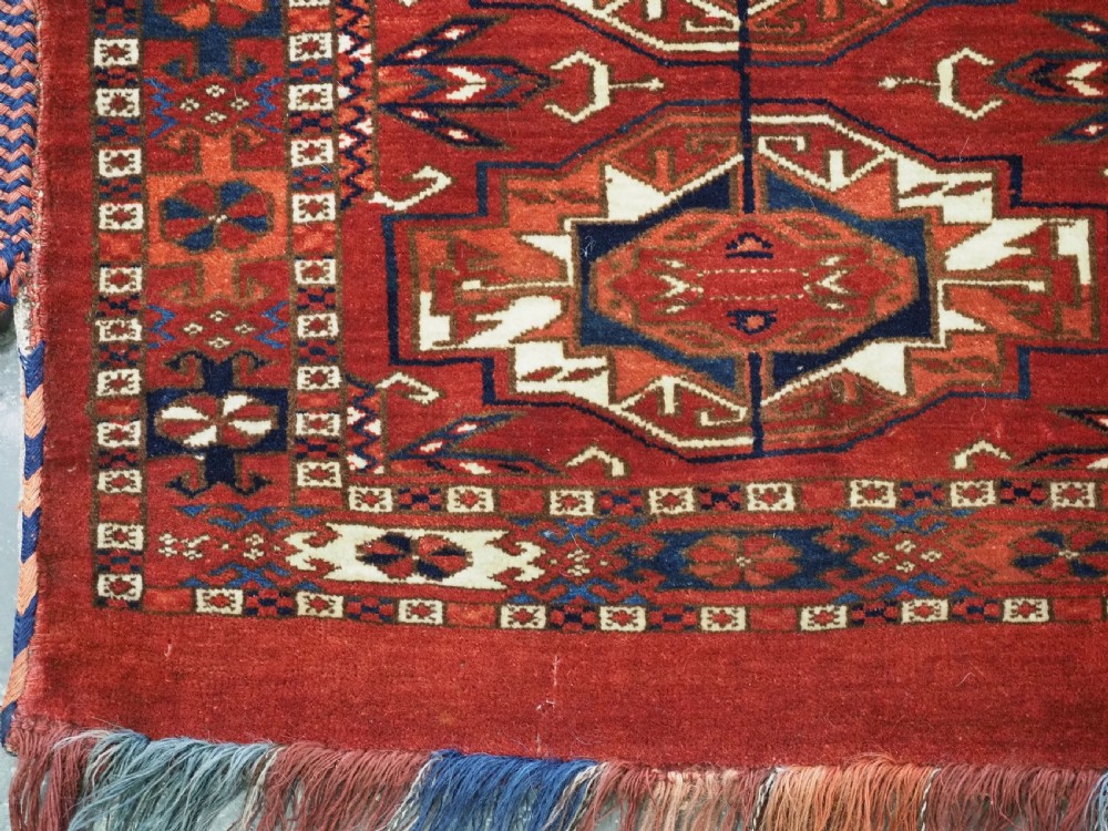 A horizontal handwoven wool Tekke Turkmen torba featuring six octagonal gul medallions on a deep red background with geometric borders and braided side tassels. View VIII