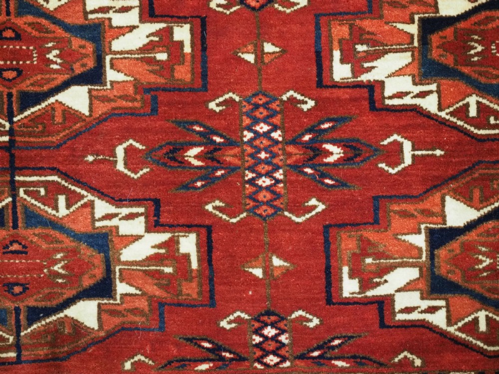 A horizontal handwoven wool Tekke Turkmen torba featuring six octagonal gul medallions on a deep red background with geometric borders and braided side tassels. View IX
