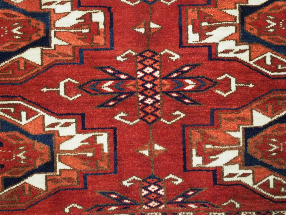A horizontal handwoven wool Tekke Turkmen torba featuring six octagonal gul medallions on a deep red background with geometric borders and braided side tassels. View X