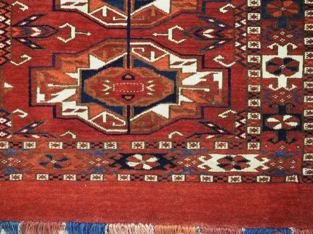 A horizontal handwoven wool Tekke Turkmen torba featuring six octagonal gul medallions on a deep red background with geometric borders and braided side tassels. View XI
