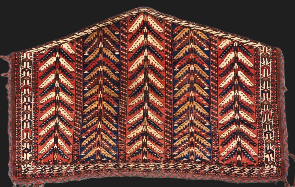 A pentagonal antique Turkmen wool textile featuring vertical rows of white and gold chevron leaf motifs on a dark red background framed by geometric borders.