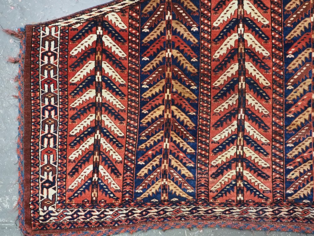 A pentagonal antique Turkmen wool textile featuring vertical rows of white and gold chevron leaf motifs on a dark red background framed by geometric borders. View III