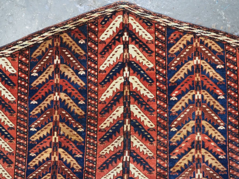 A pentagonal antique Turkmen wool textile featuring vertical rows of white and gold chevron leaf motifs on a dark red background framed by geometric borders. View IV