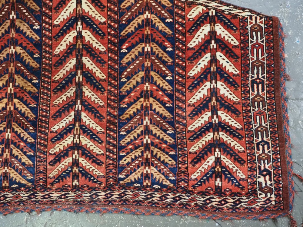 A pentagonal antique Turkmen wool textile featuring vertical rows of white and gold chevron leaf motifs on a dark red background framed by geometric borders. View V