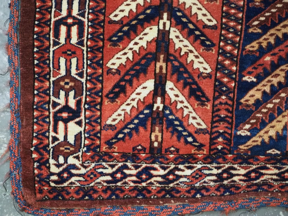 A pentagonal antique Turkmen wool textile featuring vertical rows of white and gold chevron leaf motifs on a dark red background framed by geometric borders. View VII