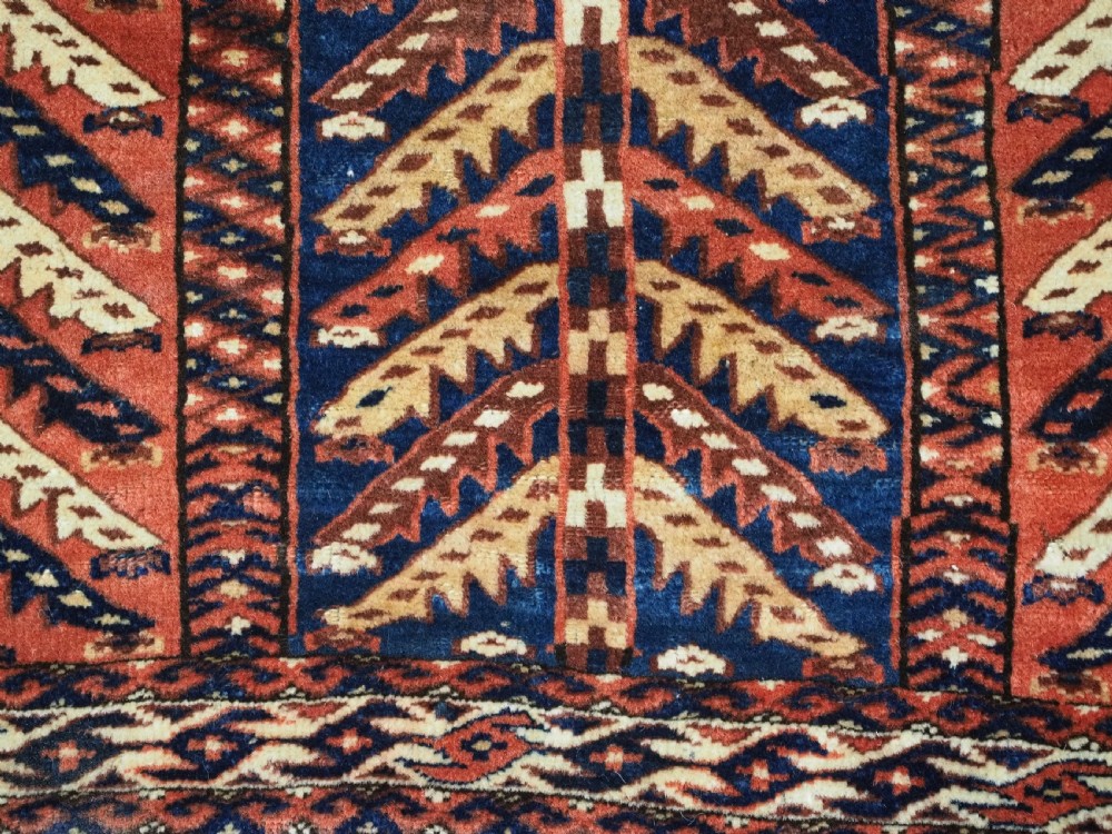 A pentagonal antique Turkmen wool textile featuring vertical rows of white and gold chevron leaf motifs on a dark red background framed by geometric borders. View VIII