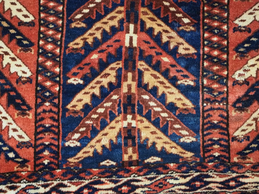 A pentagonal antique Turkmen wool textile featuring vertical rows of white and gold chevron leaf motifs on a dark red background framed by geometric borders. View IX