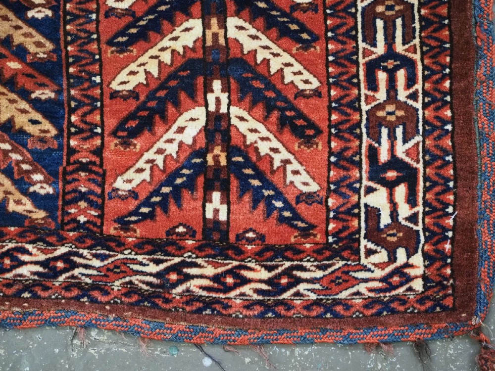 A pentagonal antique Turkmen wool textile featuring vertical rows of white and gold chevron leaf motifs on a dark red background framed by geometric borders. View X