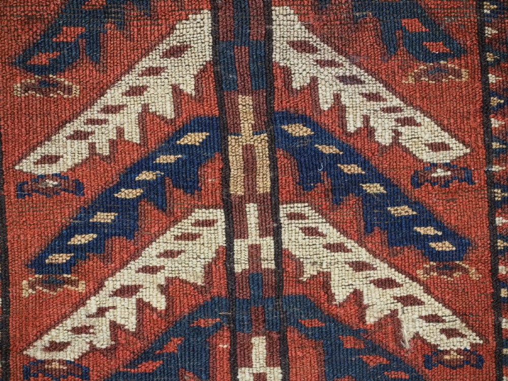 A pentagonal antique Turkmen wool textile featuring vertical rows of white and gold chevron leaf motifs on a dark red background framed by geometric borders. View XI
