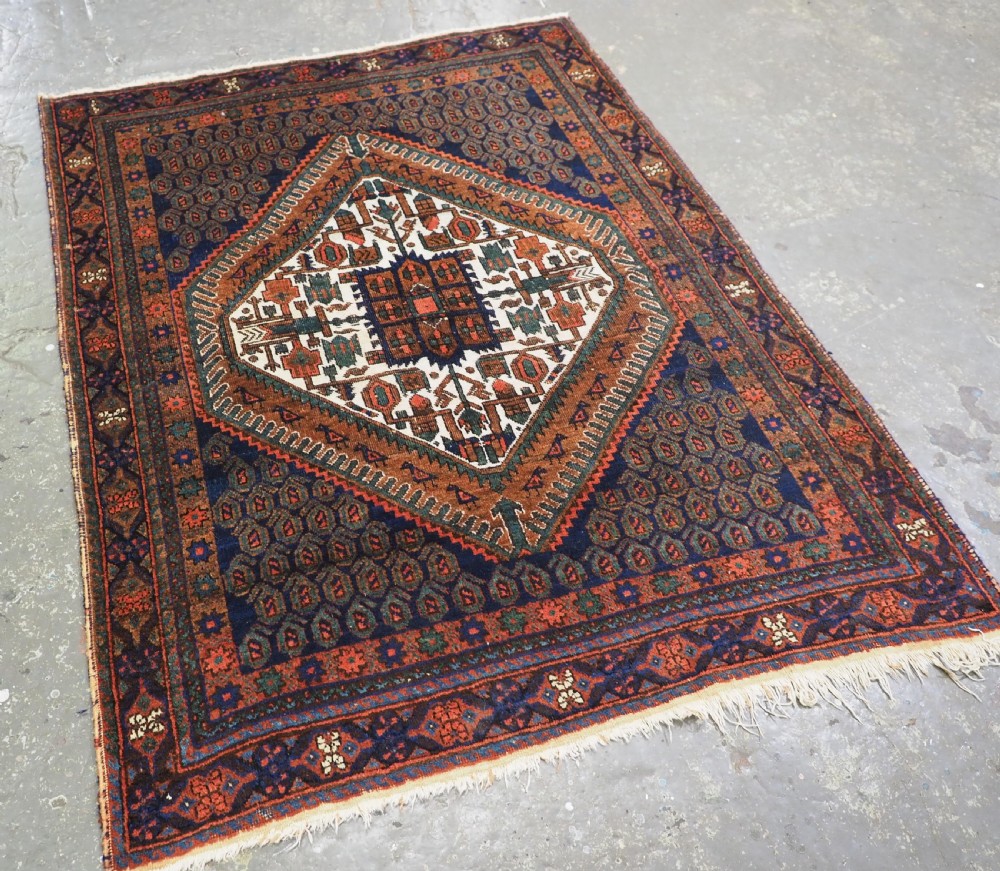 An antique hand-knotted wool rug featuring a central diamond-shaped medallion on a dark indigo field filled with repeating boteh motifs and geometric borders. View II