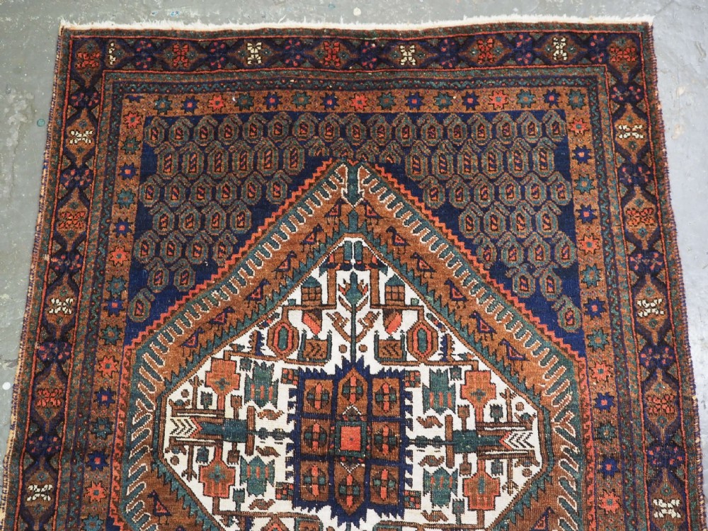 An antique hand-knotted wool rug featuring a central diamond-shaped medallion on a dark indigo field filled with repeating boteh motifs and geometric borders. View III