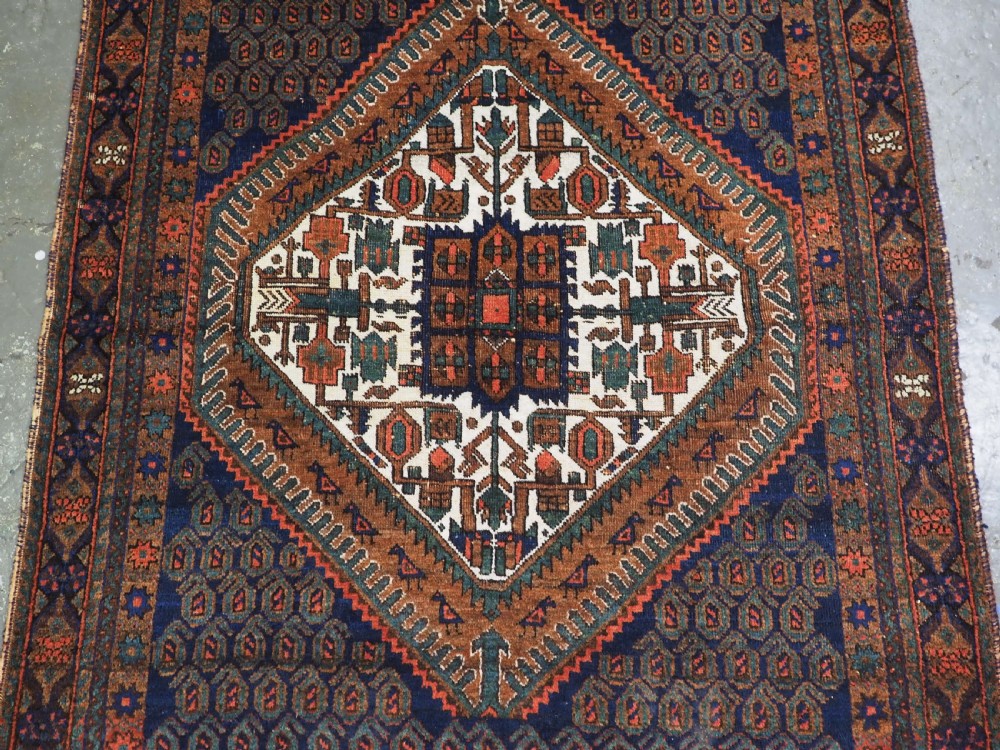 An antique hand-knotted wool rug featuring a central diamond-shaped medallion on a dark indigo field filled with repeating boteh motifs and geometric borders. View IV