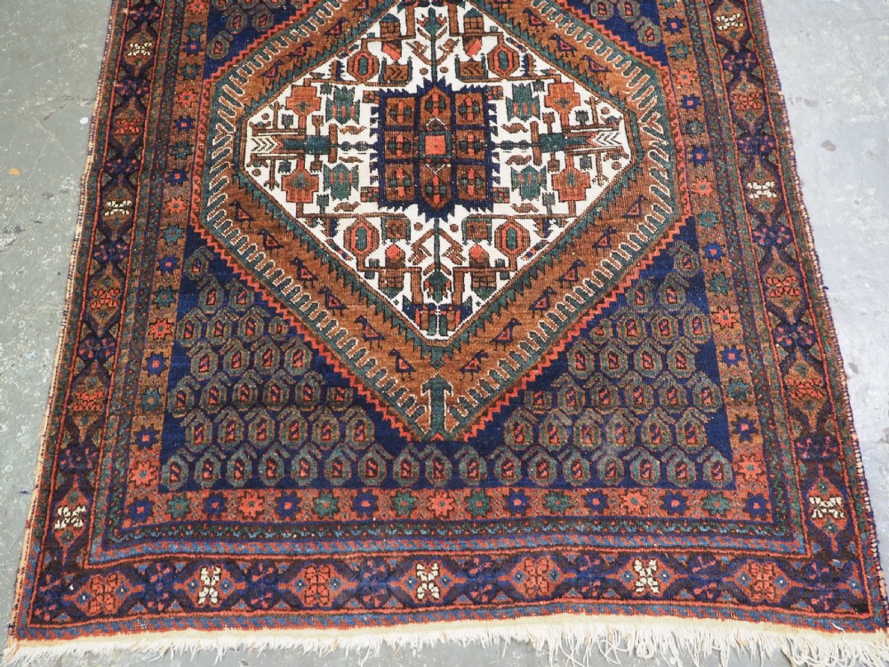 An antique hand-knotted wool rug featuring a central diamond-shaped medallion on a dark indigo field filled with repeating boteh motifs and geometric borders. View V