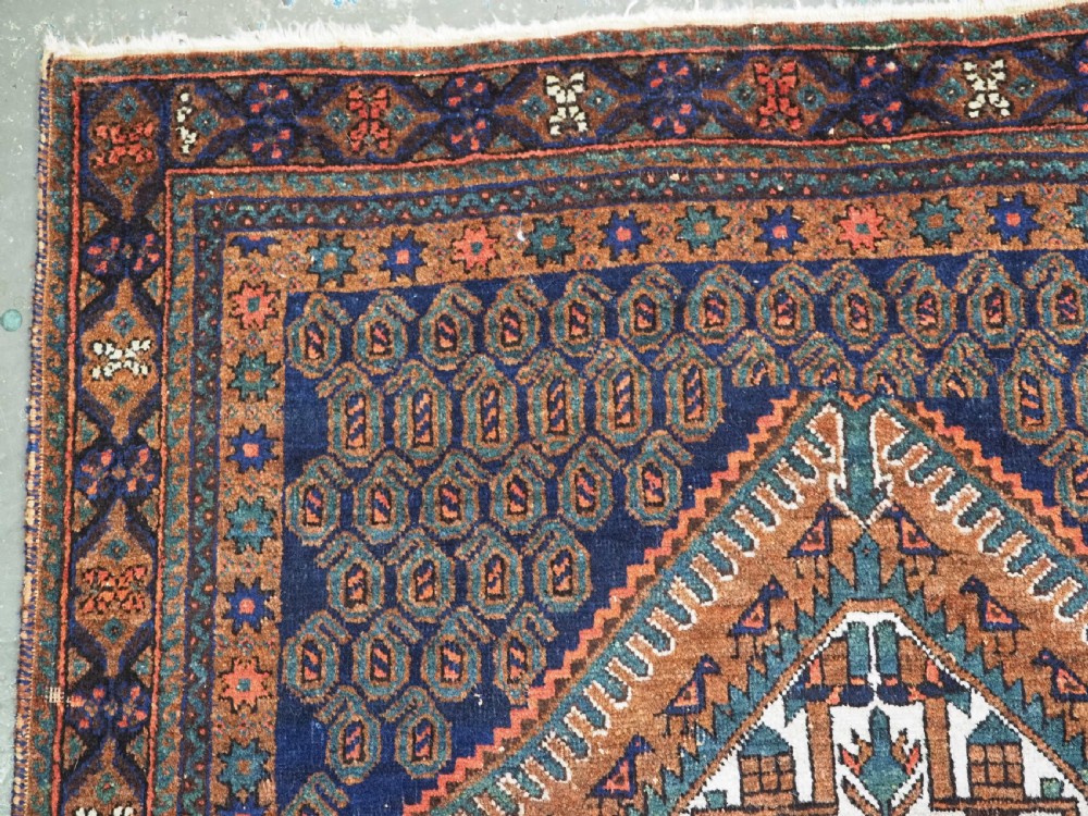 An antique hand-knotted wool rug featuring a central diamond-shaped medallion on a dark indigo field filled with repeating boteh motifs and geometric borders. View VI