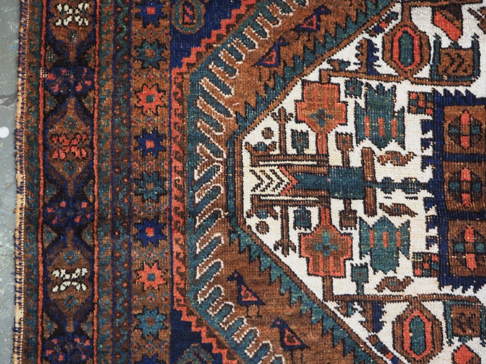 An antique hand-knotted wool rug featuring a central diamond-shaped medallion on a dark indigo field filled with repeating boteh motifs and geometric borders. View VII