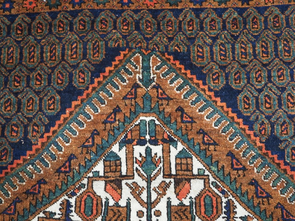 An antique hand-knotted wool rug featuring a central diamond-shaped medallion on a dark indigo field filled with repeating boteh motifs and geometric borders. View VIII