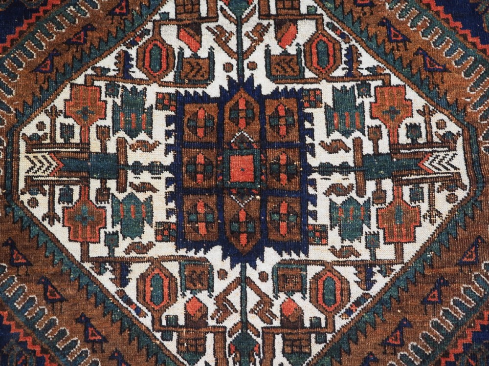 An antique hand-knotted wool rug featuring a central diamond-shaped medallion on a dark indigo field filled with repeating boteh motifs and geometric borders. View IX
