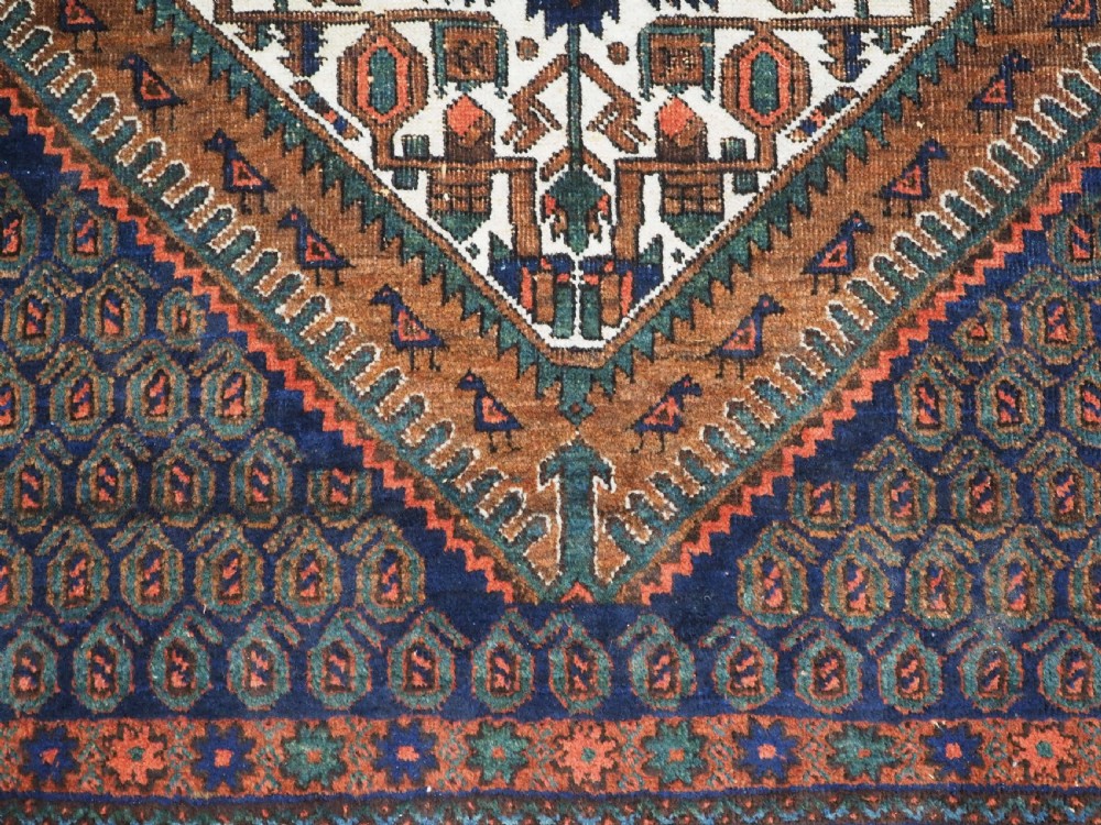An antique hand-knotted wool rug featuring a central diamond-shaped medallion on a dark indigo field filled with repeating boteh motifs and geometric borders. View X