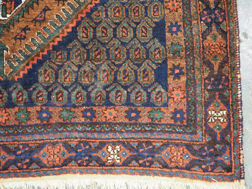 An antique hand-knotted wool rug featuring a central diamond-shaped medallion on a dark indigo field filled with repeating boteh motifs and geometric borders. View XI