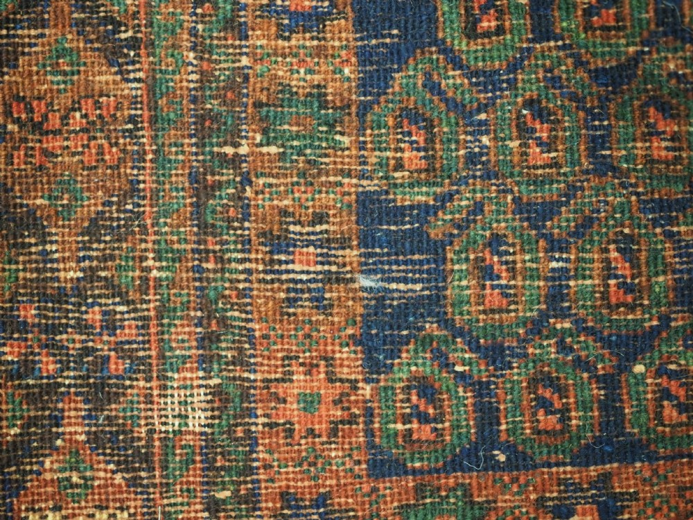 An antique hand-knotted wool rug featuring a central diamond-shaped medallion on a dark indigo field filled with repeating boteh motifs and geometric borders. View XII