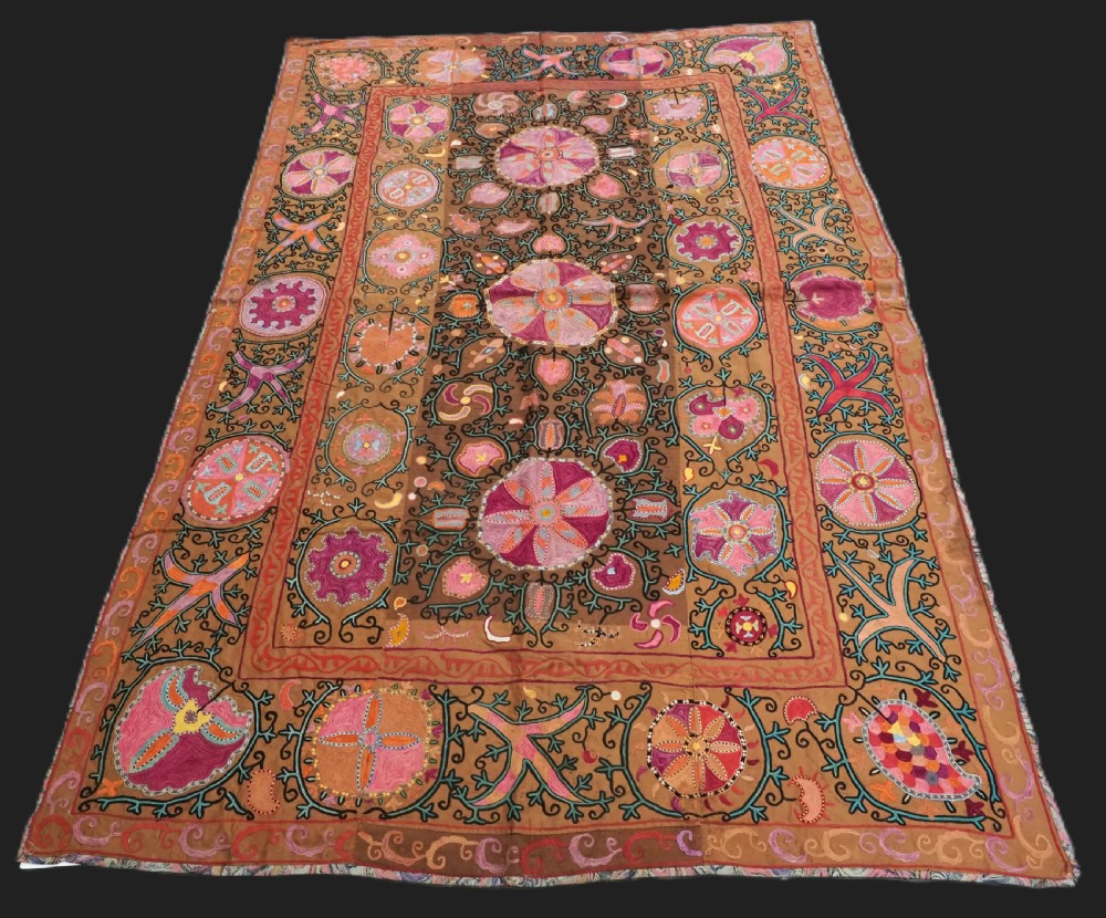 An antique Uzbek Shahrisabz region suzani textile with pink and orange silk embroidered floral medallions on a brown cotton field.