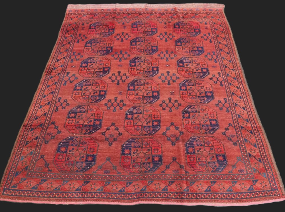 An antique Ersari Turkmen hand-knotted wool main carpet featuring a terracotta red ground filled with dark blue octagonal gul motifs and framed by geometric borders.