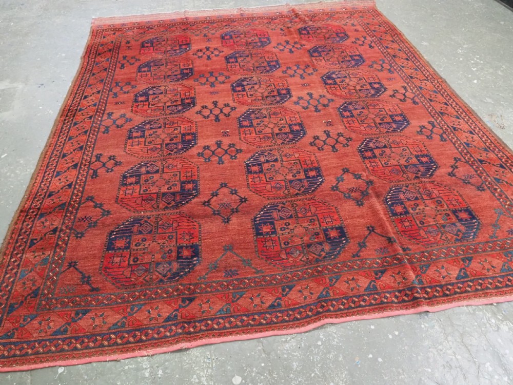 An antique Ersari Turkmen hand-knotted wool main carpet featuring a terracotta red ground filled with dark blue octagonal gul motifs and framed by geometric borders. View II
