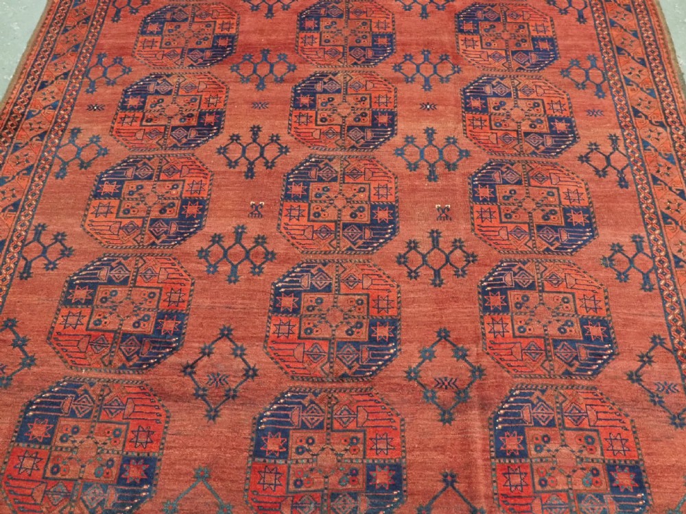 An antique Ersari Turkmen hand-knotted wool main carpet featuring a terracotta red ground filled with dark blue octagonal gul motifs and framed by geometric borders. View IV