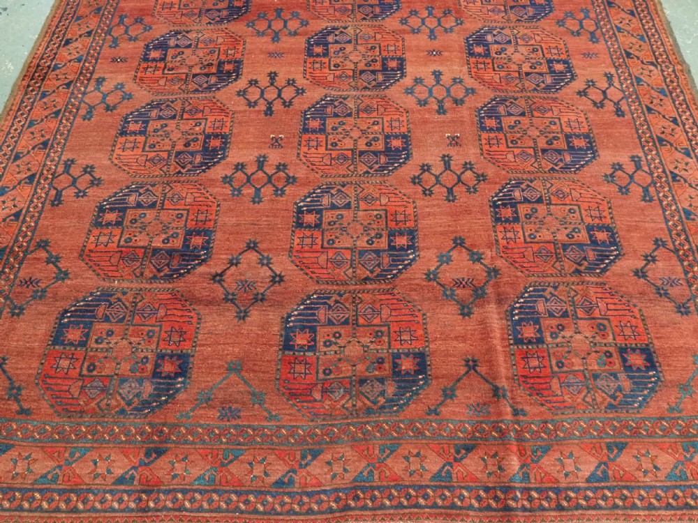 An antique Ersari Turkmen hand-knotted wool main carpet featuring a terracotta red ground filled with dark blue octagonal gul motifs and framed by geometric borders. View V