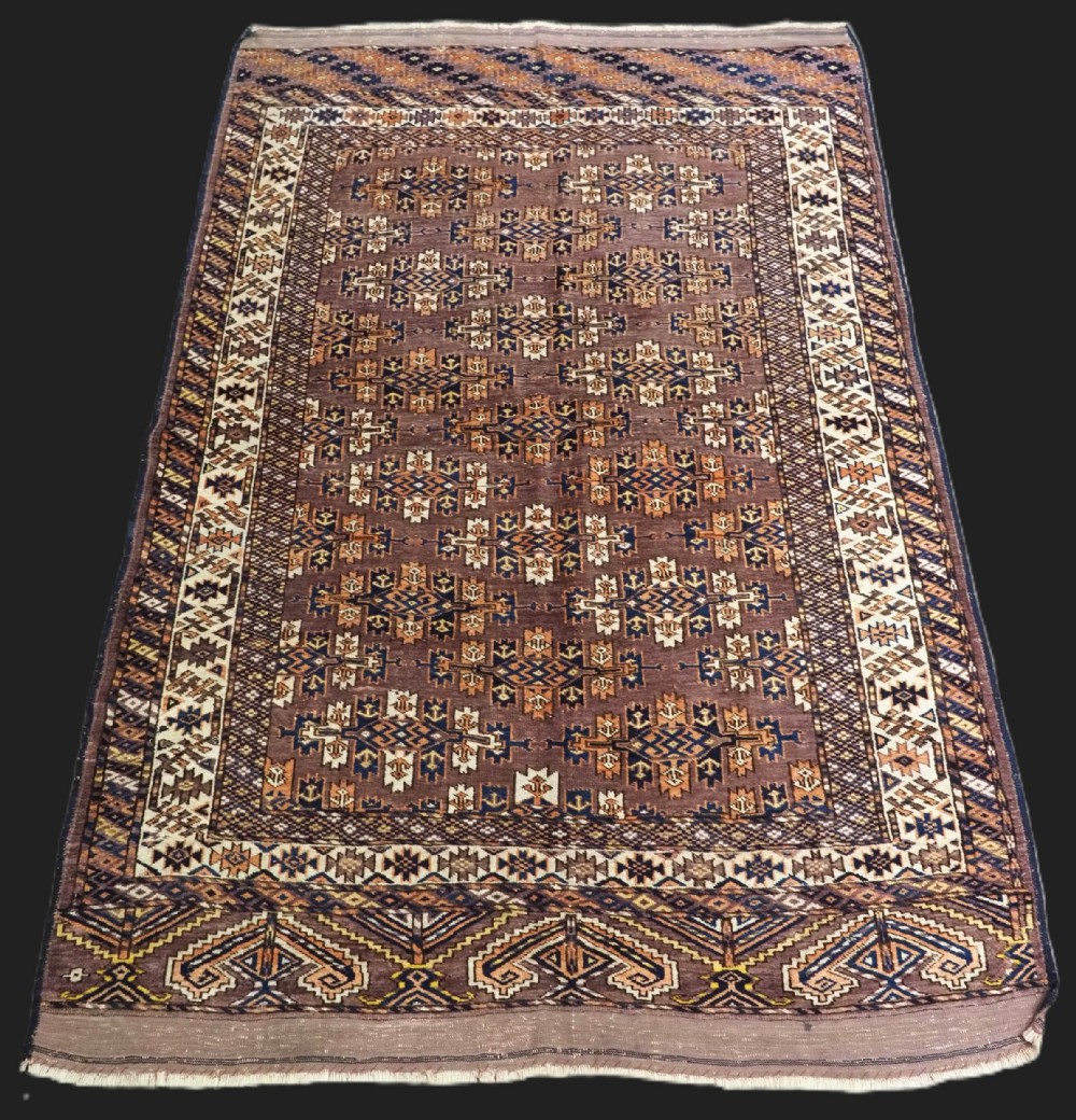 An antique hand-knotted wool carpet featuring repeated diamond-shaped kepse gul motifs across a dark aubergine field, framed by geometric borders.
