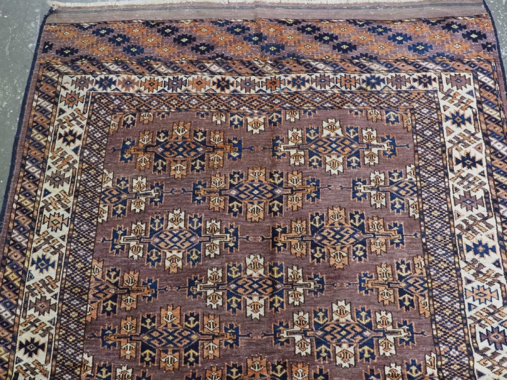 An antique hand-knotted wool carpet featuring repeated diamond-shaped kepse gul motifs across a dark aubergine field, framed by geometric borders. View III