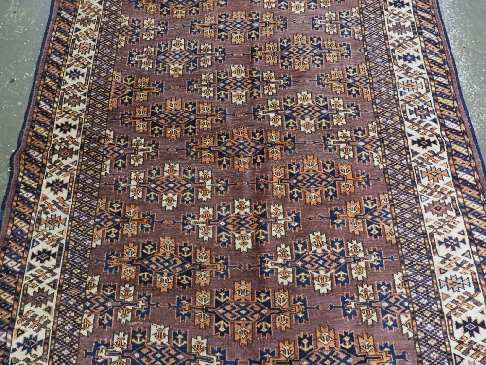 An antique hand-knotted wool carpet featuring repeated diamond-shaped kepse gul motifs across a dark aubergine field, framed by geometric borders. View IV