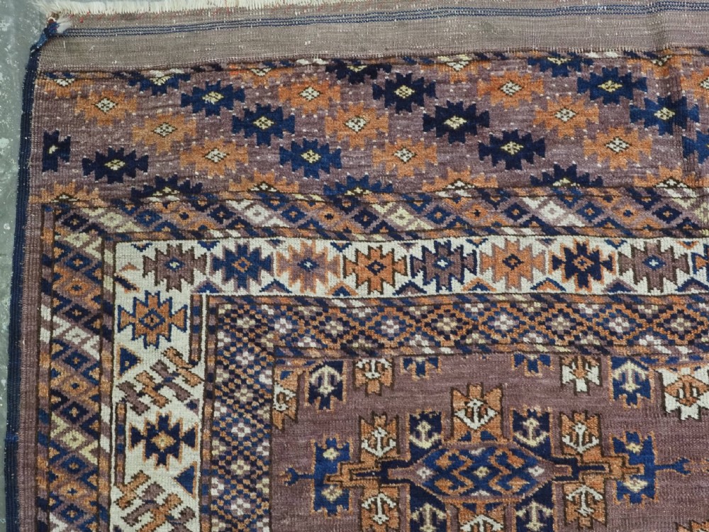 An antique hand-knotted wool carpet featuring repeated diamond-shaped kepse gul motifs across a dark aubergine field, framed by geometric borders. View V