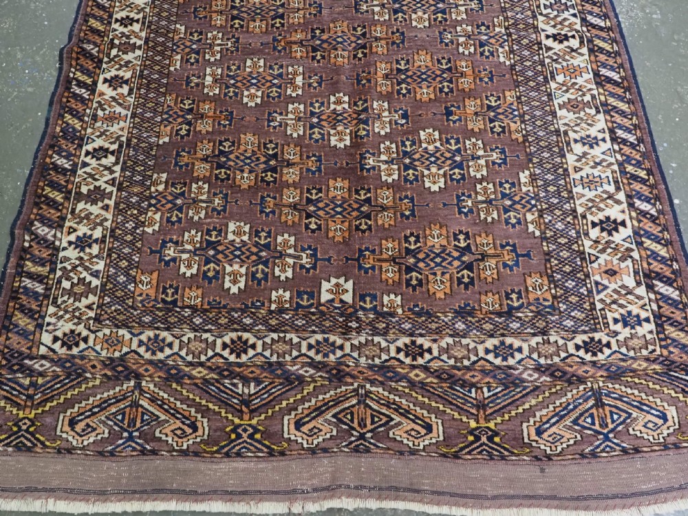 An antique hand-knotted wool carpet featuring repeated diamond-shaped kepse gul motifs across a dark aubergine field, framed by geometric borders. View VI