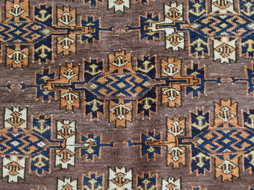 An antique hand-knotted wool carpet featuring repeated diamond-shaped kepse gul motifs across a dark aubergine field, framed by geometric borders. View IX