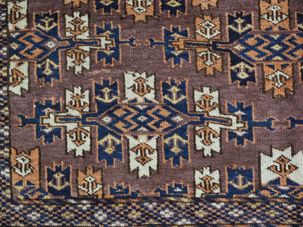 An antique hand-knotted wool carpet featuring repeated diamond-shaped kepse gul motifs across a dark aubergine field, framed by geometric borders. View X