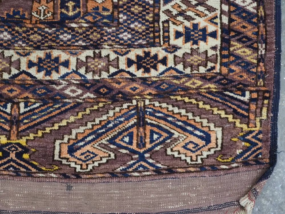 An antique hand-knotted wool carpet featuring repeated diamond-shaped kepse gul motifs across a dark aubergine field, framed by geometric borders. View XI