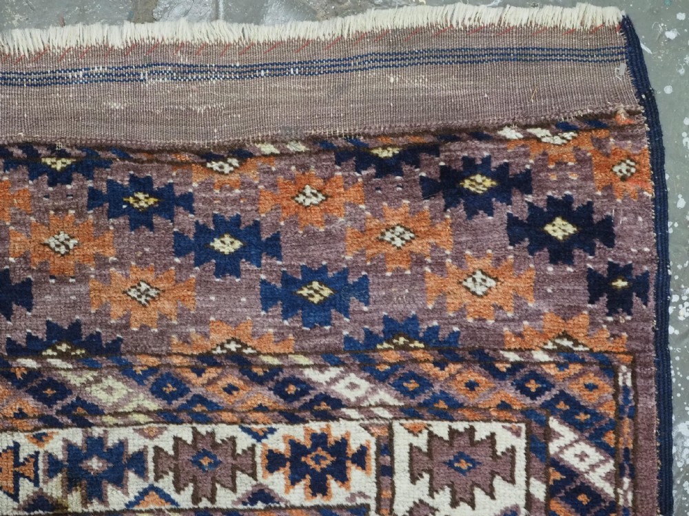 An antique hand-knotted wool carpet featuring repeated diamond-shaped kepse gul motifs across a dark aubergine field, framed by geometric borders. View XII